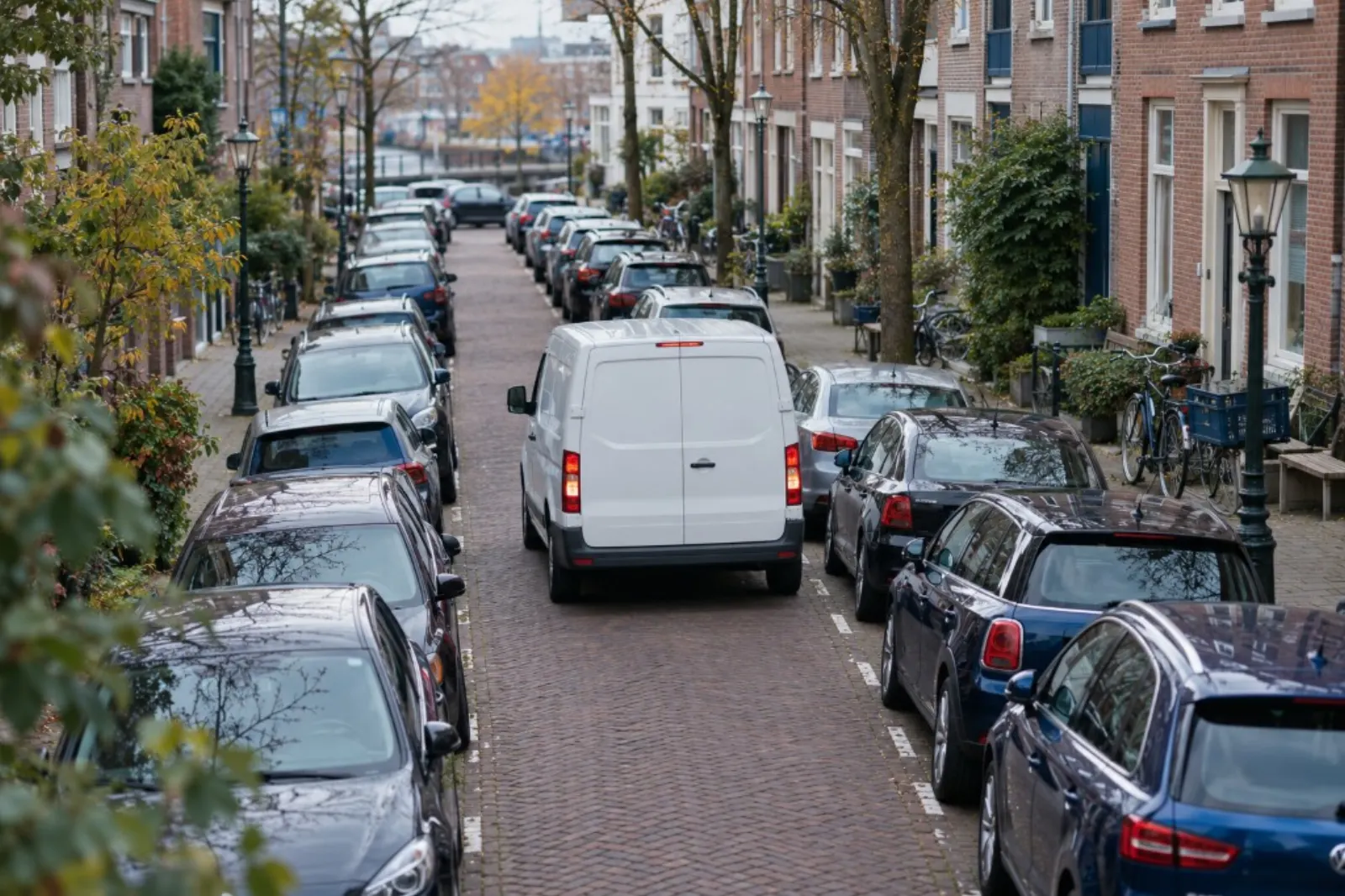 Witte bestelbus rijdt door een smalle straat met geparkeerde auto's aan weerszijden